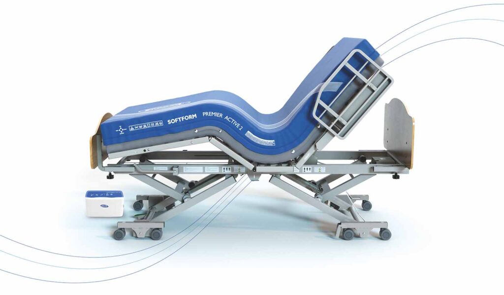 Image of a hospital bed with a blue mattress. The bed features an adjustable frame that allows the head and foot sections to be elevated, enhancing patient comfort. The bed is shown raised on its wheeled base, with side rails for added patient safety.
