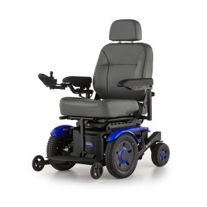 A blue and black electric wheelchair with a padded grey seat and backrest. The wheelchair features armrests, a joystick control on the right armrest, and four wheels with thick treads, two larger rear wheels and two smaller front wheels.