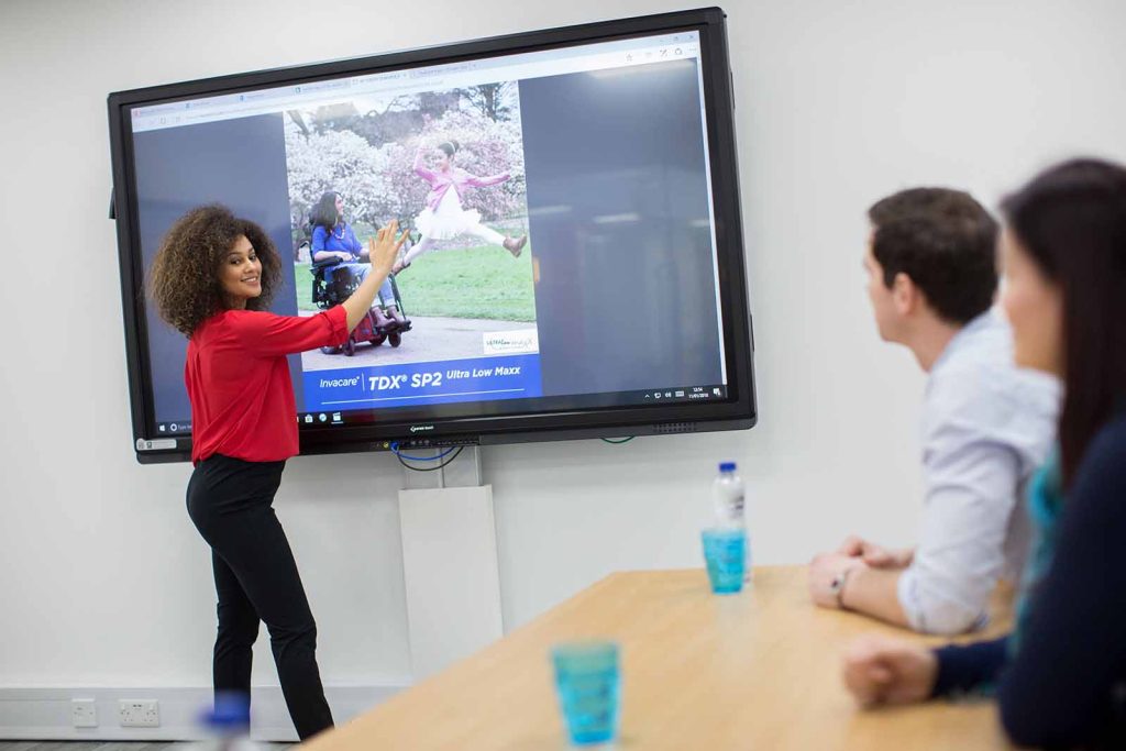 Woman demonstrating Invacare education resources on large screen to a classroom of adults